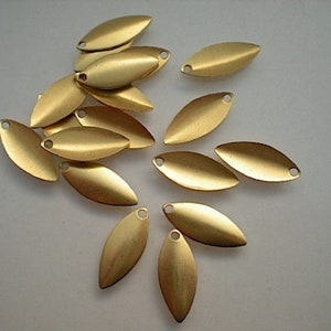 May include: A group of 17 gold-colored metal leaf-shaped charms with a hole at the top. The charms are scattered on a white surface.