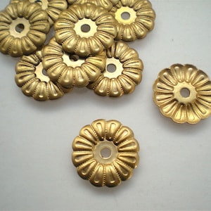 May include: A collection of small, gold-colored metal flower-shaped components. Each component has a central hole and a ridged, petal-like design around the edge. The components are scattered on a light background.