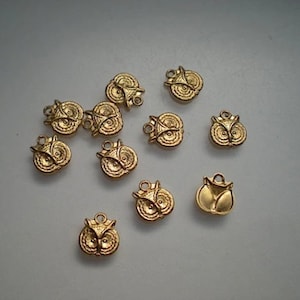 Può includere: Una collezione di dieci ciondoli a forma di gufo color oro. I ciondoli sono dettagliati con rilievi e hanno un anello per attaccarli a gioielli o altri oggetti artigianali.