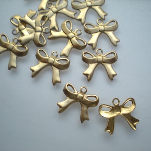 Könnte beinhalten: Eine Gruppe von 12 goldfarbenen Metall-Schleifenanhängern. Die Schleifen sind alle gleich groß und gleich geformt und haben oben eine Schlaufe zum Anbringen an einer Halskette, einem Armband oder anderem Schmuck.