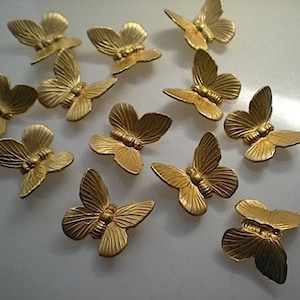 May include: A collection of small, gold-colored butterfly embellishments. Each butterfly has detailed wing patterns and a textured body. The butterflies are arranged on a light-colored surface, showcasing their metallic sheen. These decorative elements are ideal for craft projects.