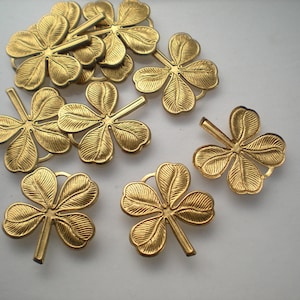Könnte beinhalten: Zehn goldfarbene Glückskleeblatt-Anhänger. Die Anhänger sind aus Metall und haben eine strukturierte Oberfläche.