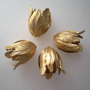 May include: Four gold-colored metal flower-shaped embellishments. Each embellishment has a textured surface and a pointed tip.