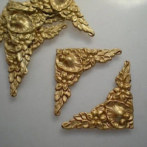 May include: Several ornate, gold-colored corner embellishments. Each piece features a floral design with detailed leaves and flowers. The castings are likely made of metal and are suitable for decorative applications in furniture or crafts.