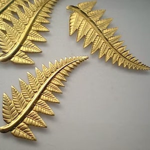 May include: Three gold-colored metal fern leaf shapes. The leaves are detailed with a textured pattern.