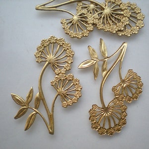May include: Gold-colored metal floral embellishments in various designs. The pieces feature detailed flower and leaf patterns, with a matte finish. The arrangement includes several individual floral elements, suitable for crafting or decorative purposes.