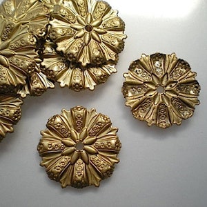 Peut inclure: Plusieurs ornements floraux décoratifs en métal doré antique. Chaque pièce présente un trou central et des motifs détaillés en forme de pétales. Les ornements sont disposés sur une surface blanche.