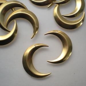 May include: A group of gold-colored crescent moon charms with a hole at the top for hanging. The charms are made of metal and have a smooth, shiny finish.
