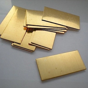 May include: A collection of rectangular, gold-coloured metal plates. The plates are arranged in a scattered pile, with some overlapping. The surface of the plates appears smooth and reflective, with subtle variations in colour and texture.