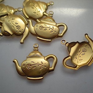 May include: Several gold-colored metal teapot charms with floral details. Each charm has a loop for attaching to jewelry or other crafts. The teapots have a classic design with a handle, spout, and lid.