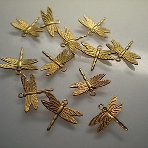 Könnte beinhalten: Eine Sammlung kleiner, goldfarbener Libellen-Anhänger. Jeder Anhänger hat detaillierte Flügel und eine Schlaufe zum Befestigen an Schmuck oder anderen Bastelarbeiten. Die Libellen sind auf einer hellen Oberfläche angeordnet.