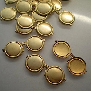 May include: A group of gold-colored metal round glasses with a hinge on each side. The glasses are arranged in a pile on a white surface.