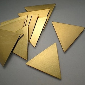 May include: A group of 14 gold-coloured metal triangle shapes. The triangles are arranged in a random pattern on a white surface.