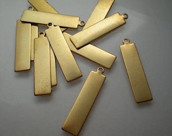 May include: A collection of rectangular, gold-colored metal tags with a small loop at one end. The tags have a matte finish and appear to be blank, suitable for engraving or stamping. The tags are scattered across a light-colored surface.