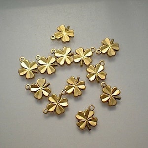 May include: A group of 12 gold-coloured four-leaf clover charms with a loop at the top for attaching to jewellery or other crafts.