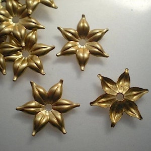 Puede incluir: Primer plano de varios componentes metálicos dorados en forma de flor de seis pétalos. Cada componente tiene un agujero central y probablemente se utiliza para la fabricación de joyas u otros proyectos de artesanía. Los pétalos tienen una forma ligeramente redondeada.