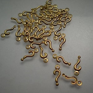 Könnte beinhalten: Eine große Gruppe goldener Fragezeichen-Anhänger. Die Anhänger sind aus Metall und haben eine glänzende Oberfläche. Sie sind perfekt, um Schmuck oder Bastelarbeiten eine Prise Verspieltheit zu verleihen.