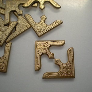 Peut inclure: Un tas de coins de métal de couleur or avec un motif orné. Les coins sont disposés de manière aléatoire sur une surface blanche.