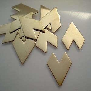 May include: A group of ten gold-colored metal arrow shapes, some are stacked on top of each other, and some are laying flat on a white surface.