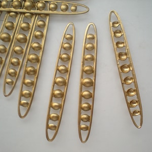 May include: A set of gold-colored metal pea pod shapes with rounded edges. Each pod is made up of a series of small, round beads.
