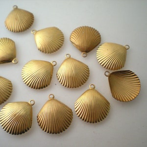 May include: A collection of gold-colored seashell charms. Each charm has a detailed, ridged texture and a small loop at the top for attaching to jewelry or other crafts. The charms are arranged on a white surface.