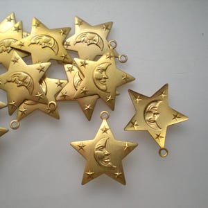 May include: A collection of gold-colored star-shaped charms. Each charm features a crescent moon with a smiling face, surrounded by smaller star accents. The charms have a loop for hanging.
