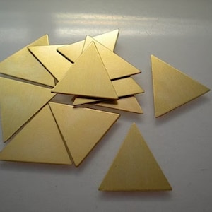 May include: A group of 10 gold-colored metal triangle shapes. The triangles are arranged in a random pattern on a white surface.