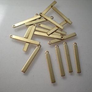 Puede incluir: Un montón de colgantes de barra de metal dorado con un bucle en la parte superior. Los colgantes miden aproximadamente 2,5 cm de largo y 0,6 cm de ancho.