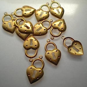 May include: A group of 10 gold heart-shaped lock charms with keyholes. The charms are scattered on a white surface.