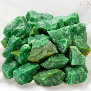 Puede incluir: Un montón de piedras de aventurina verde en bruto. Las piedras varían en tamaño y forma, con una superficie texturizada y un color verde vibrante. La imagen está sobre un fondo blanco, con el texto "LIMRA DESIGNS" en la esquina superior derecha.