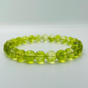 May include: A bracelet made of translucent, lime-green beads. The beads are spherical and strung together to form a complete circle. The bracelet is displayed against a white backdrop, accentuating the vivid colour and texture of the beads.