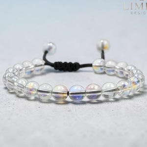 May include: A clear beaded bracelet with iridescent spheres and a black adjustable cord. The bracelet features a sliding knot closure and is set against a light gray background. The brand name "LIMRA DESIGNS" is in the upper right corner.