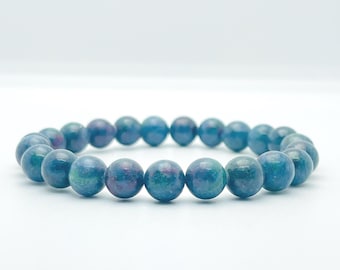 May include: A stretch bracelet composed of round, polished beads in shades of deep teal, blue, and hints of magenta. The beads are uniform in size and arranged in a circular loop, showcasing a smooth, glossy texture with natural color variations.