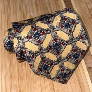 Peut inclure: Une cravate roulée avec un motif géométrique. La cravate présente un motif répétitif de formes jaunes, grises, rouges et bleues. La cravate est faite d'un tissu lisse et convient aux occasions formelles.