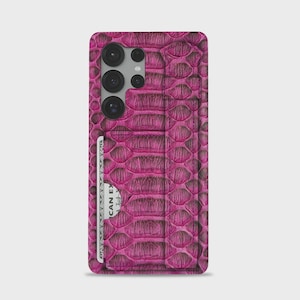 May include: A magenta phone case with a textured, snake-skin pattern. The case has a built-in card holder with a visible credit card. The phone case has a camera module with three lenses.