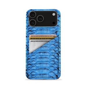 Puede incluir: Una funda de teléfono azul con textura de piel de serpiente y un tarjetero incorporado. La funda tiene un módulo de cámara negro con tres lentes y un flash. Dos tarjetas son parcialmente visibles en el tarjetero.