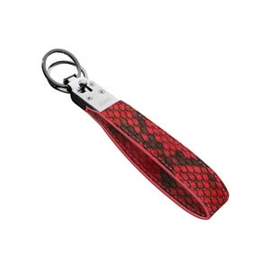 May include: A red and brown snakeskin-patterned keychain wrist strap with a silver-tone metal clasp and key ring. The word "VELANO" is printed on the metal clasp. The strap is made of a textured material.