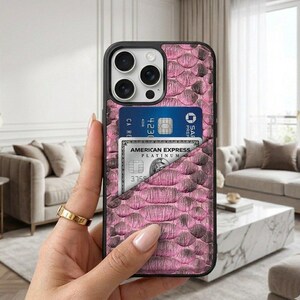 Op de afbeelding: Een roze telefoonhoesje met slangenprint en een zwarte rand. De hoes heeft een vakje met een blauwe creditcard en een American Express Platinum card. De telefoonhoes heeft een camera en een flitser.