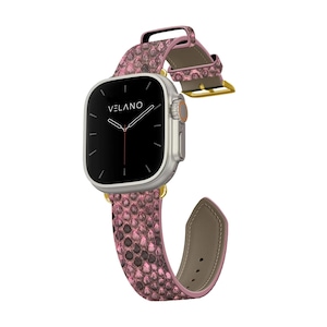 Può includere: Uno smartwatch argentato con schermo nero e cinturino rosa con motivo a pelle di serpente. Il cinturino ha una fibbia dorata e un retro in pelle. Il quadrante mostra il marchio "VELANO".