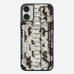 Pode incluir: Capa de smartphone com padrão de pele de cobra em tons de cinza e preto. A capa tem um porta-cartões embutido com um cartão parcialmente visível. As bordas da capa são pretas.