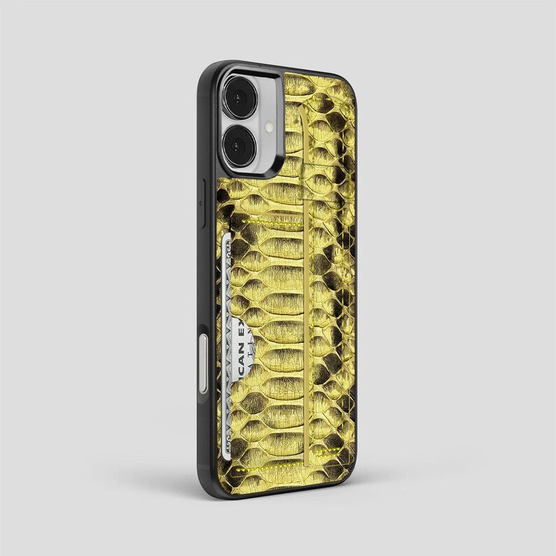 Peut inclure: Coque de t&eacute;l&eacute;phone noire avec un motif peau de serpent dor&eacute;. L'&eacute;tui comporte une fente pour carte avec une carte de cr&eacute;dit blanche partiellement visible. La coque est con&ccedil;ue pour un smartphone.