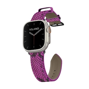 May include: A silver smartwatch with a black screen and the brand name "VELANO" is displayed. The watch features a vibrant pink snakeskin-patterned band. The band is attached to the watch with a black clasp.