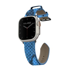 Puede incluir: Un reloj inteligente plateado con pantalla negra y correa azul con estampado de piel de serpiente. La esfera muestra la marca "VELANO". La correa es de material texturizado y tiene cierre de hebilla.