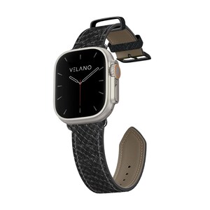 May include: A silver smartwatch with a black woven leather band. The watch face is black with white markings and the brand name "VELANO". The band is secured with a black metal clasp.