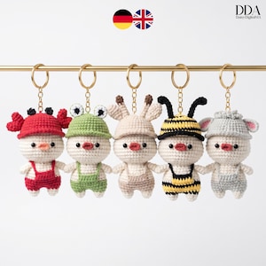 Peut inclure: Cinq porte-clés en crochet en forme de canetons, chacun avec un costume unique : un crabe, une grenouille, un lapin, une abeille et une souris. Les canetons sont blancs avec des accents rouges, verts, beiges, jaunes et gris. Chaque porte-clés a un anneau doré.