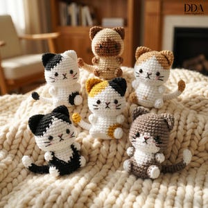 Peut inclure: Six figurines de chats crochetés de différentes couleurs, dont blanc, noir, marron et jaune. Chaque chat a un motif et une expression faciale uniques, avec de petites queues et des détails. Les chats sont disposés sur une surface texturée de couleur crème.