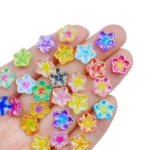 May include: A collection of small, colorful flower-shaped embellishments. Each flower has a gold outline and a translucent center in shades of pink, blue, yellow, green, and purple. These decorative elements are ideal for crafts.