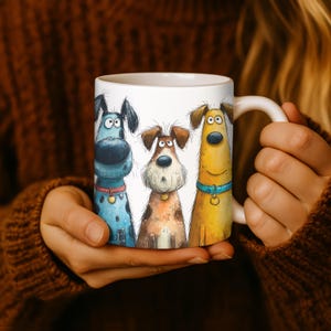 May include: A white ceramic mug featuring a whimsical illustration of three cartoon dogs. The dogs are in shades of blue, brown, and yellow, each with unique expressions and wearing collars. The mug has a curved handle and is held by a person.