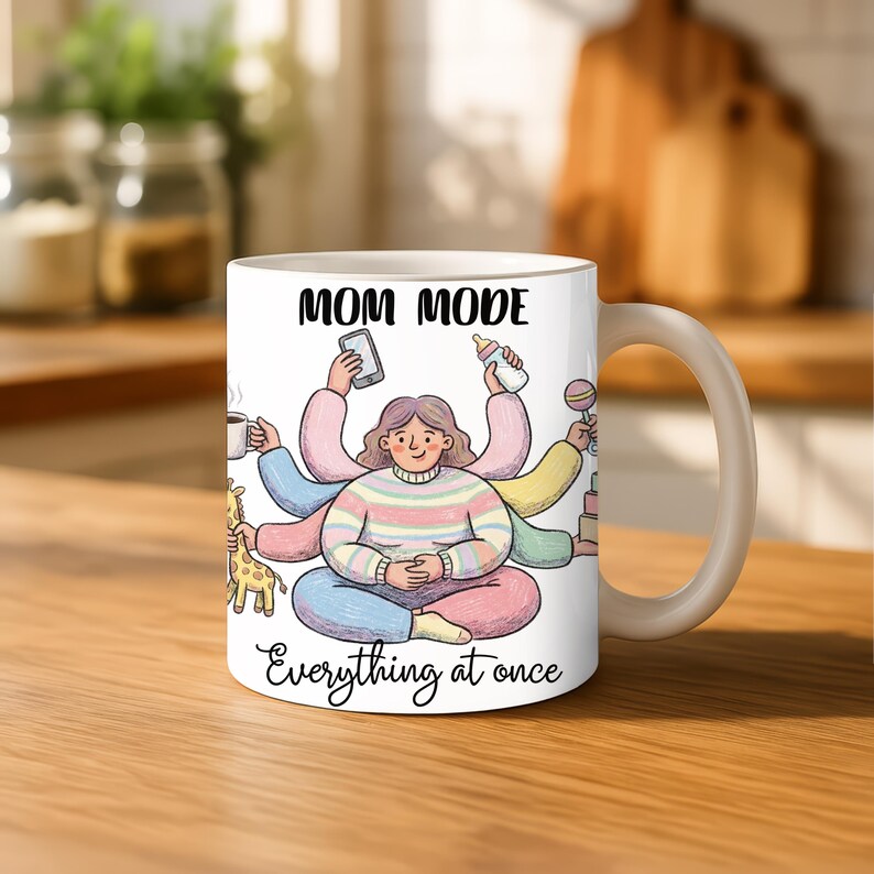 K&ouml;nnte beinhalten: Wei&szlig;e Keramik-Tasse mit den Worten "MOM MODE" und "Everything at once" aufgedruckt. Die Tasse zeigt eine Cartoon-Illustration einer Frau mit mehreren Armen, die verschiedene Gegenst&auml;nde h&auml;lt, darunter ein Telefon, eine Babyflasche und eine Kaffeetasse.