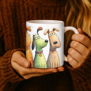 May include: White ceramic mug featuring a whimsical illustration of three cartoon dogs in shades of brown and green. The dogs have expressive eyes and are wearing collars. The mug is held by a person wearing a brown sweater.